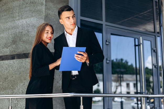 Zakelijke partners man en vrouw naast een bedrijfsgebouw met een document. - Afbeelding