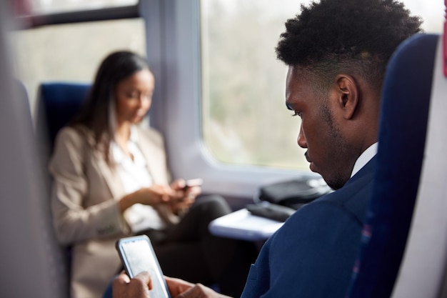 Zakelijke passagiers zitten in de trein pendelen naar het werk kijken naar mobiele telefoons