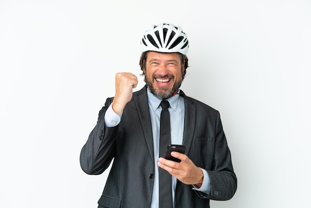 Zakelijke senior man met een fietshelm geïsoleerd op een witte achtergrond met telefoon in overwinningspositie