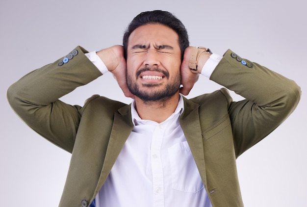 Zakelijke stress en Aziatische man bedekken oren luid en geestelijke gezondheid tegen een grijze studioachtergrond Mannelijke werknemer angstige werknemer en ondernemer met handen op tempel luidruchtig en blokkerend voor stilte