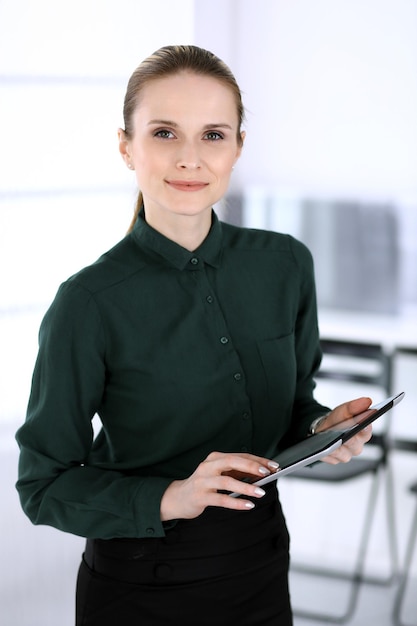 Zakelijke vrouw headshot in moderne kantoorsecretaris of vrouwelijke advocaat die tabletcomputer gebruikt terwijl ze rechtop staat Bedrijfsmensenconcept