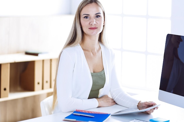 Zakelijke vrouw headshot tijdens het werken met de computer aan de balie in moderne kantoren. Ontwerper of vrouwelijke advocaat ziet er prachtig uit in witte vrijetijdskleding. Mensen bedrijfsconcept.