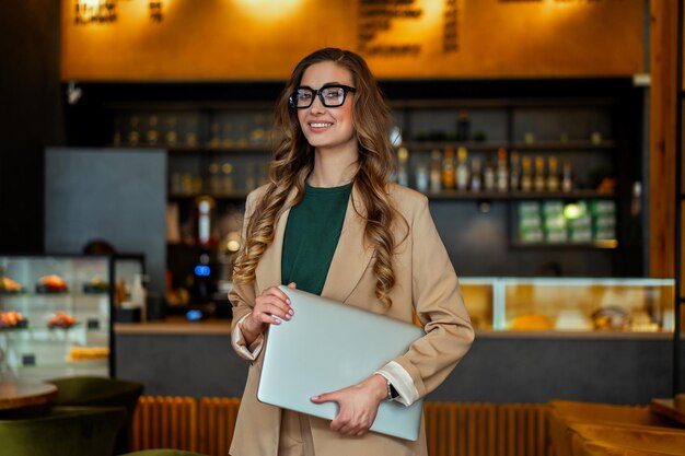 Zakelijke vrouw restauranteigenaar met Laptop In handen gekleed elegante broekpak staande In Restaurant met toog achtergrond Kaukasische vrouwelijke glazen zakenman binnen