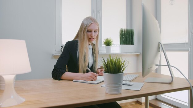 Zakelijke vrouw schrijft in een boek op tafel terwijl ze tegen het raam in het kantoor zit