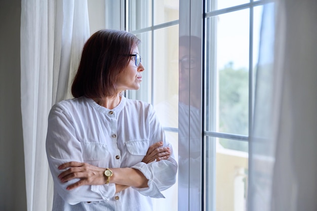 Zakelijke vrouw van middelbare leeftijd kijkt uit het raam