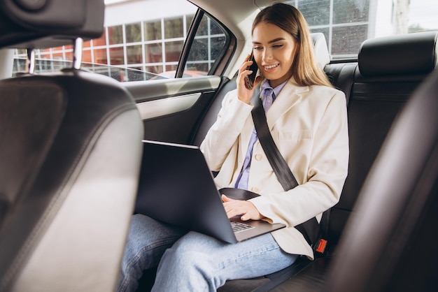 Zakelijke vrouw werkt aan een laptop in de auto terwijl ze aan het bellen is