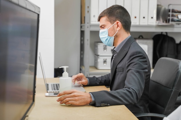 Zakelijke werknemer met gezichtsmasker weer aan het werk op kantoor na afsluiting met ontsmettingsgel