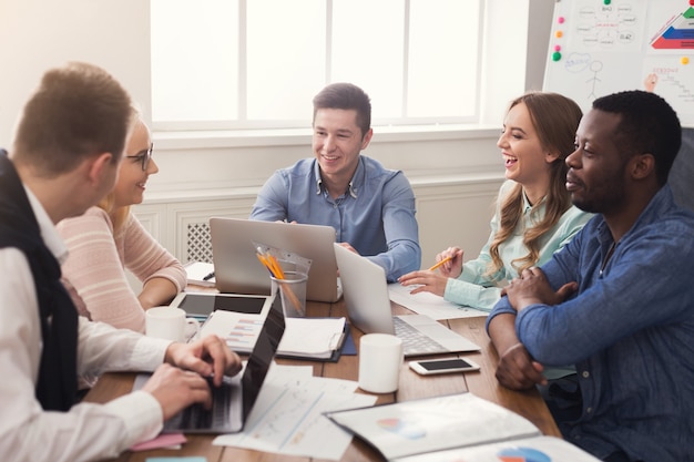 Zakelijke zakelijke bijeenkomst van multi-etnisch team. Jonge vrolijke mensen brainstormen, bespreken nieuw opstartproject op kantoor, kopiëren ruimte