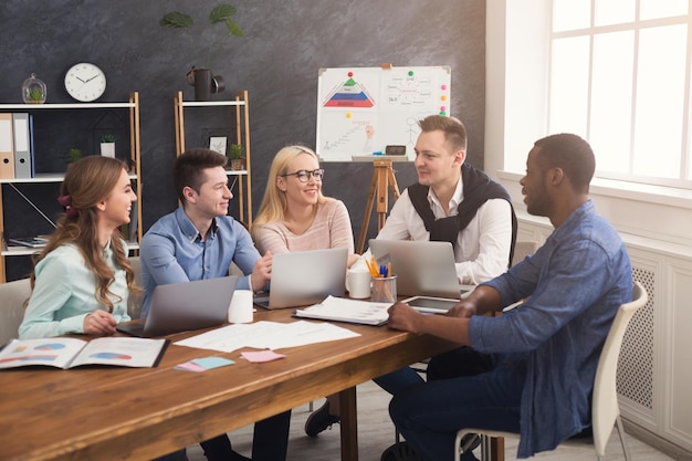 Zakelijke zakelijke bijeenkomst van multi-etnisch team. Jonge vrolijke mensen brainstormen, bespreken nieuw opstartproject op kantoor, kopiëren ruimte