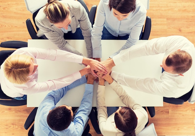 zaken, mensen, samenwerking en teamwerkconcept - close-up van creatief team dat aan tafel zit en elkaars hand vasthoudt op kantoor