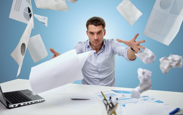 zaken, mensen, stress, emoties en mislukt concept - boze zakenman die papieren op kantoor gooit over blauwe achtergrond
