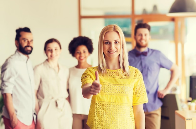 Foto zaken, opstarten, mensen, gebaar en groepswerkconcept - gelukkige jonge vrouw die duimen toont over creatief team in bureau