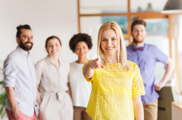 zaken, opstarten, mensen, gebaar en teamwork concept - gelukkige jonge vrouw wijzende vinger naar jou over creatief team in kantoor