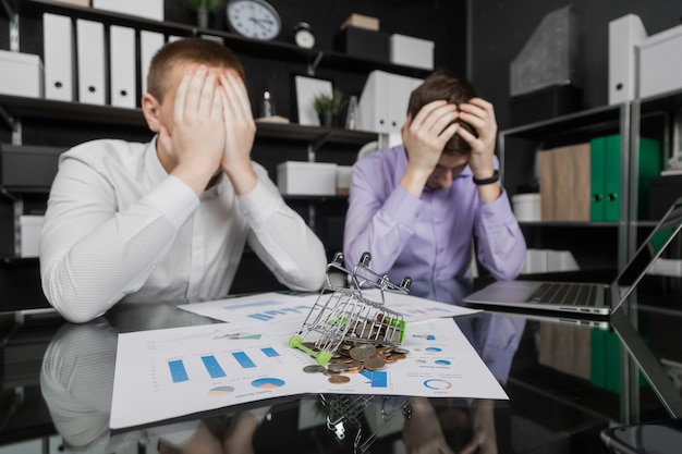 Zakenlieden grepen zijn hoofd naast het gevallen Dummy-winkelwagentje met verspreide munten