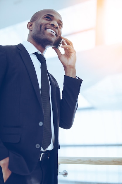 Zakenman aan de telefoon. lage hoekmening van vrolijke jonge afrikaanse man in formalwear die op de mobiele telefoon praat en glimlacht