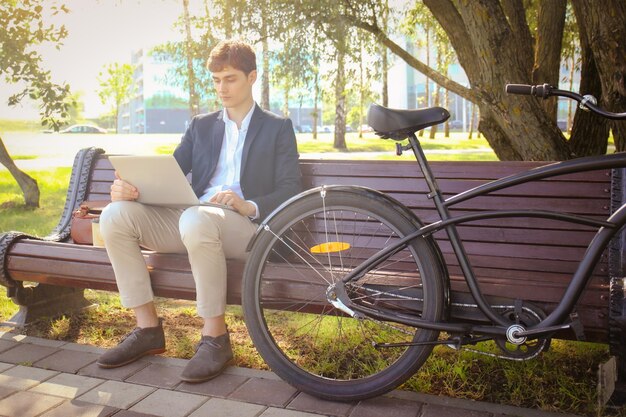 Zakenman aan een koffiepauze Hij zit op een bankje en werkt op een laptop naast de fiets