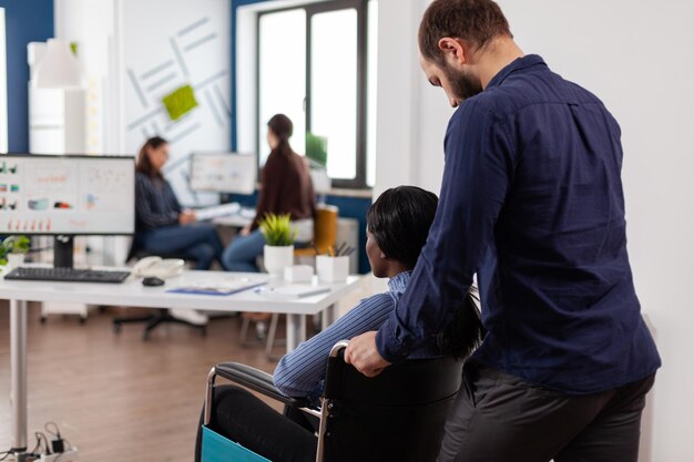 Zakenman brengen verlamde gehandicapte afro-amerikaanse zakenvrouw aan het werk in het hoofdkantoor van het opstarten van een bedrijf. teamwerk werken aan managementstrategie analyseren van bedrijfsstatistieken