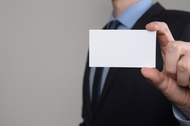 Zakenman, business man's hand houden visitekaartje tonen - close-up shot op grijze achtergrond. laat een blanco vel papier zien. papieren visitekaartje.