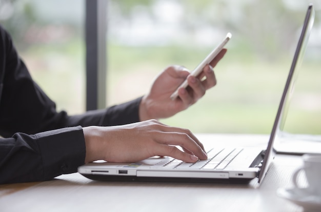 Zakenman die aan notitieboekje werken die en mobiele telefoon in koffie met koffiekop typen typen