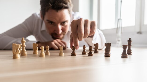 Zakenman die bedrijfsstrategie creëert door zwart-witte schaakstukken op zijn bureau te schikken.