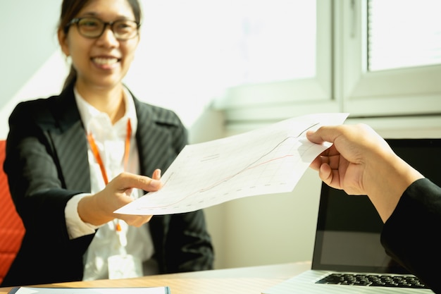 Zakenman die bij bureau met laptop werken die document grafiek overhandigen aan secretaresse.