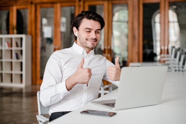 Zakenman die duimen tonen en dichtbij laptop glimlachen