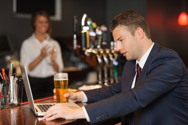 Zakenman die een bier heeft terwijl het werken aan zijn laptop