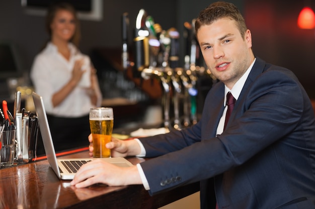 Zakenman die een pint heeft terwijl het werken aan zijn laptop