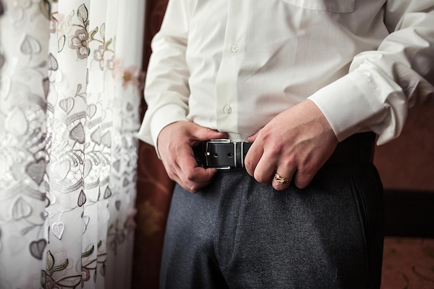 Foto zakenman die een riem omdoet, mode- en kledingconcept bruidegom maakt zich 's ochtends klaar voor de ceremonie