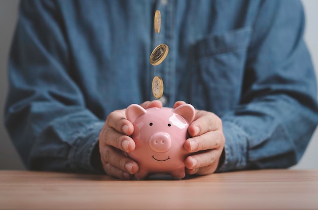 Zakenman die een roze spaarvarken vasthoudt waarvan munten vallen om geld te besparen voor investeringen en dividendrendement krijgen