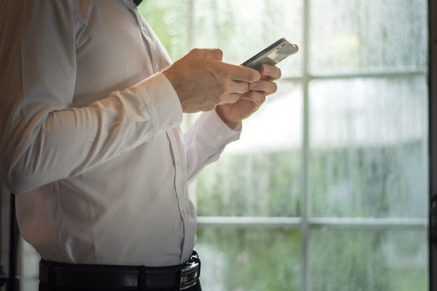 Zakenman die een slimme telefoon met behulp van terwijl status bij een venster op een regenachtige dag