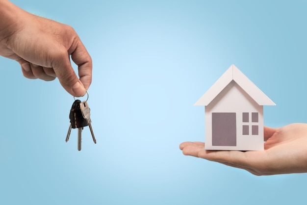 Zakenman die huissleutels en huismodel geeft aan klant op blauwe achtergrond voor herfinancieren plan en onroerend goed concept.