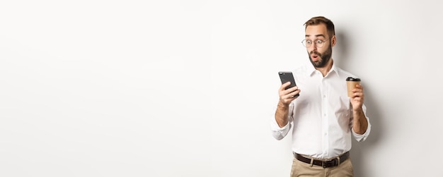 Zakenman die koffie drinkt en verbaasd kijkt naar het bericht op de mobiele telefoon die verbaasd staat over wat