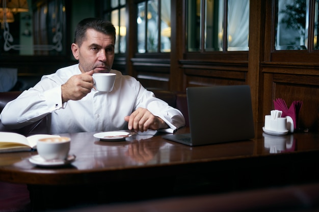 Zakenman die koffie in een koffie heeft terwijl het werken aan laptop