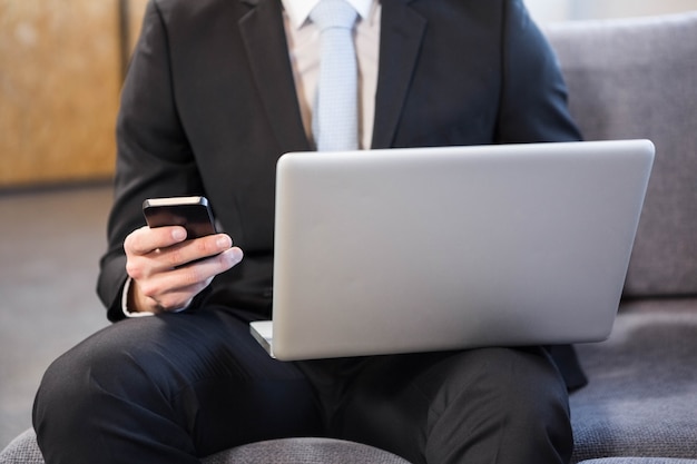 Zakenman die laptop en mobiele telefoon in bureau met behulp van