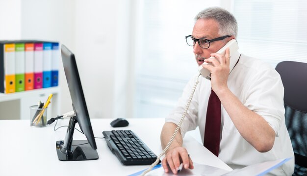 Zakenman die op de telefoon spreekt terwijl het bekijken een computermonitor in zijn bureau