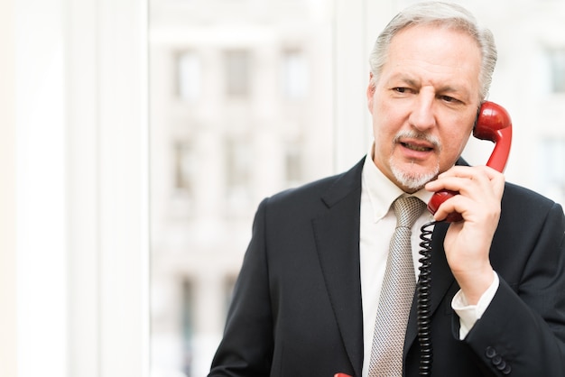 Zakenman die op een uitstekende telefoon in zijn bureau spreekt