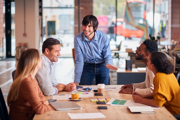 Zakenman die presentatie geeft aan collega's die rond de tafel zitten in een modern open kantoor?