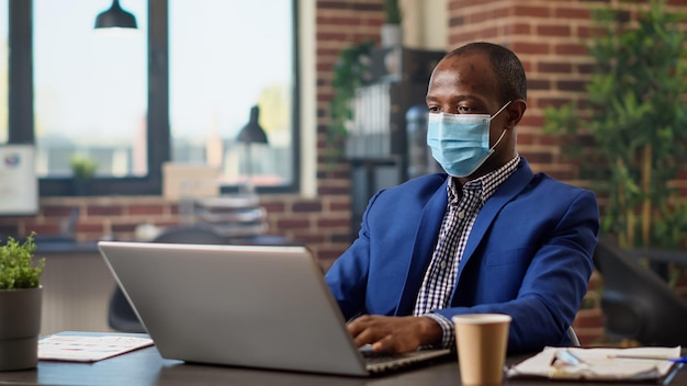 Zakenman doet informatieanalyse op laptop aan bureau, werkt in opstartkantoor tijdens covid 19 pandemie. Projectmanager die online statistieken over netwerk plant, op internet surft. Statief geschoten.