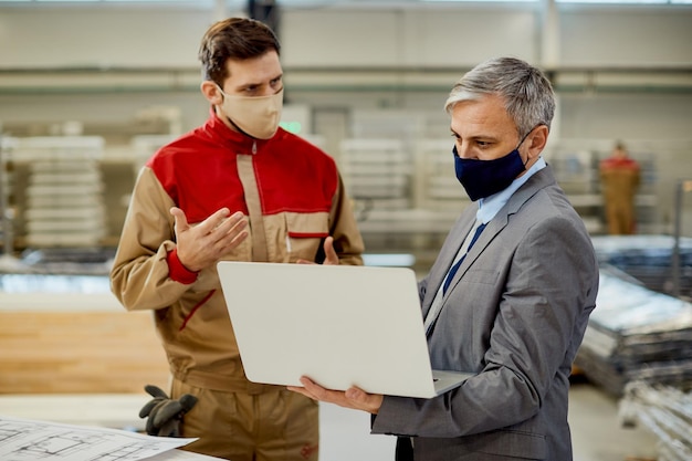 Zakenman en mannelijke werknemer met behulp van laptop tijdens het communiceren op houtbewerkingsproductiefaciliteit