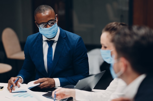 Zakenman en zakenvrouw team in medisch gezichtsmasker op kantoorvergadering. Business mensen groepsconferentie discussie met baas.