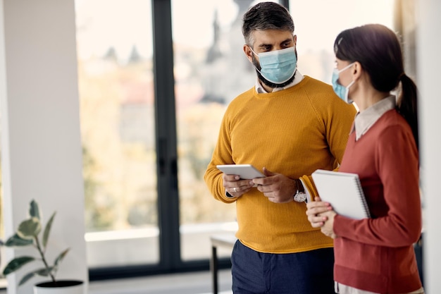 Zakenman en zijn vrouwelijke collega die gezichtsmaskers dragen tijdens het praten op kantoor