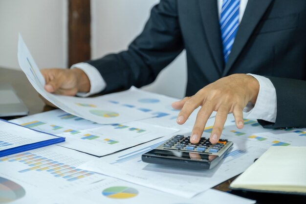 Foto zakenman hand met pen gebruik een rekenmachine en analyseer de grafiek met laptop op het thuiskantoor voor het stellen van uitdagende zakelijke doelen en het plannen om het nieuwe doel te bereiken