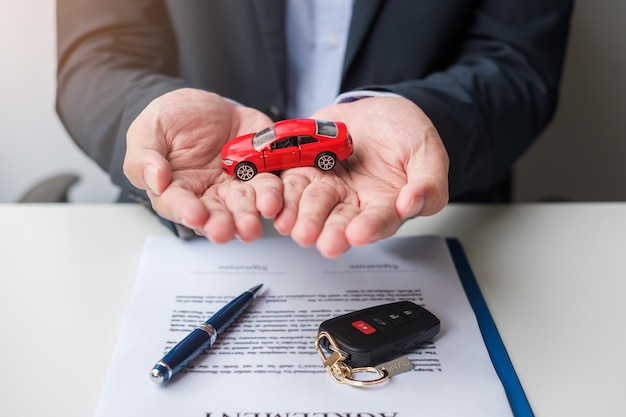 Zakenman hand met rode auto speelgoed met auto keyless pen en contract document koop en verkoop verzekering verhuur en contract overeenkomst concepten