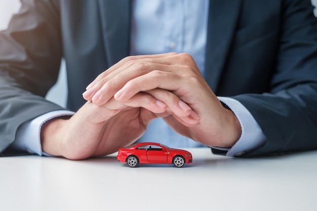 Zakenman handdekking of bescherming rode auto speelgoed op tafel Autoverzekering garantie reparatie Financieel bankieren en geld concept