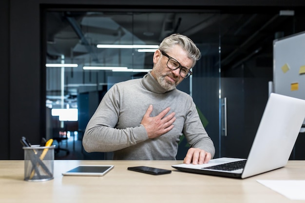 Zakenman hartaanval op werkplek volwassen grijsharige man aan het werk op laptop heeft ernstige pijn op de borst