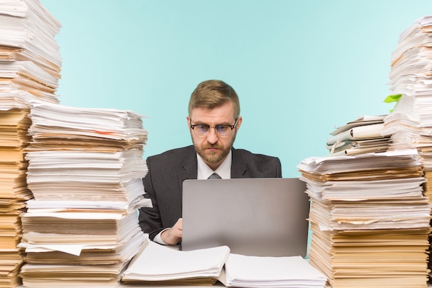 Zakenman houdt een videoconferentie op kantoor en stapels papierwerk, hij wordt overladen met werk