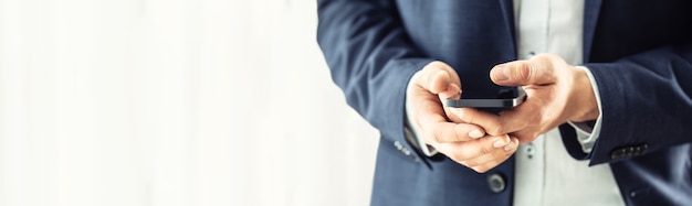 Zakenman in blauw pak met een zwarte smartphone in handen en chatten met collega's.