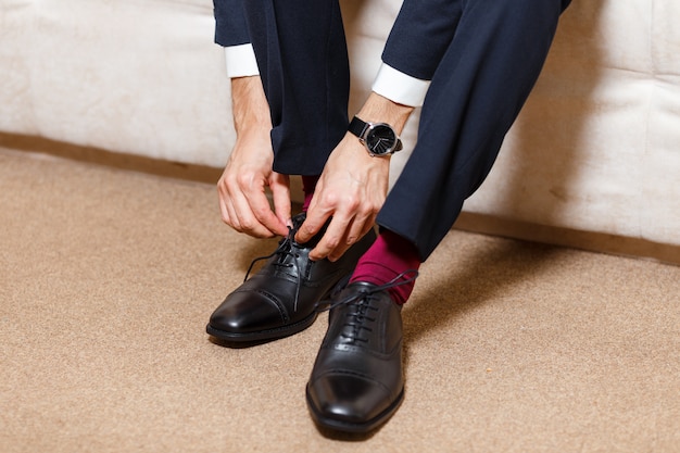Zakenman in donkerblauw pak, rode sokken en kijk hoe zijn schoenveters zwarte schoenen aan elkaar binden