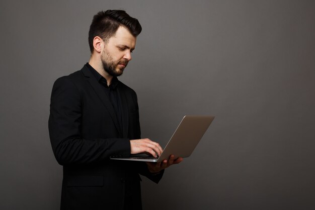 Zakenman in een elegant pak die op een laptop op een grijze achtergrond werkt